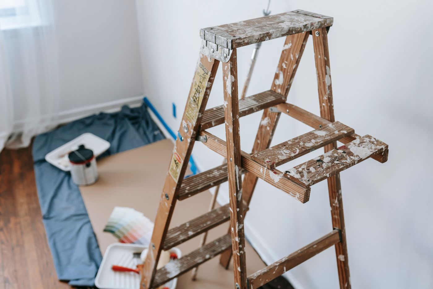 A paint-spattered wooden ladder and drop cloth in a room prepped for painting