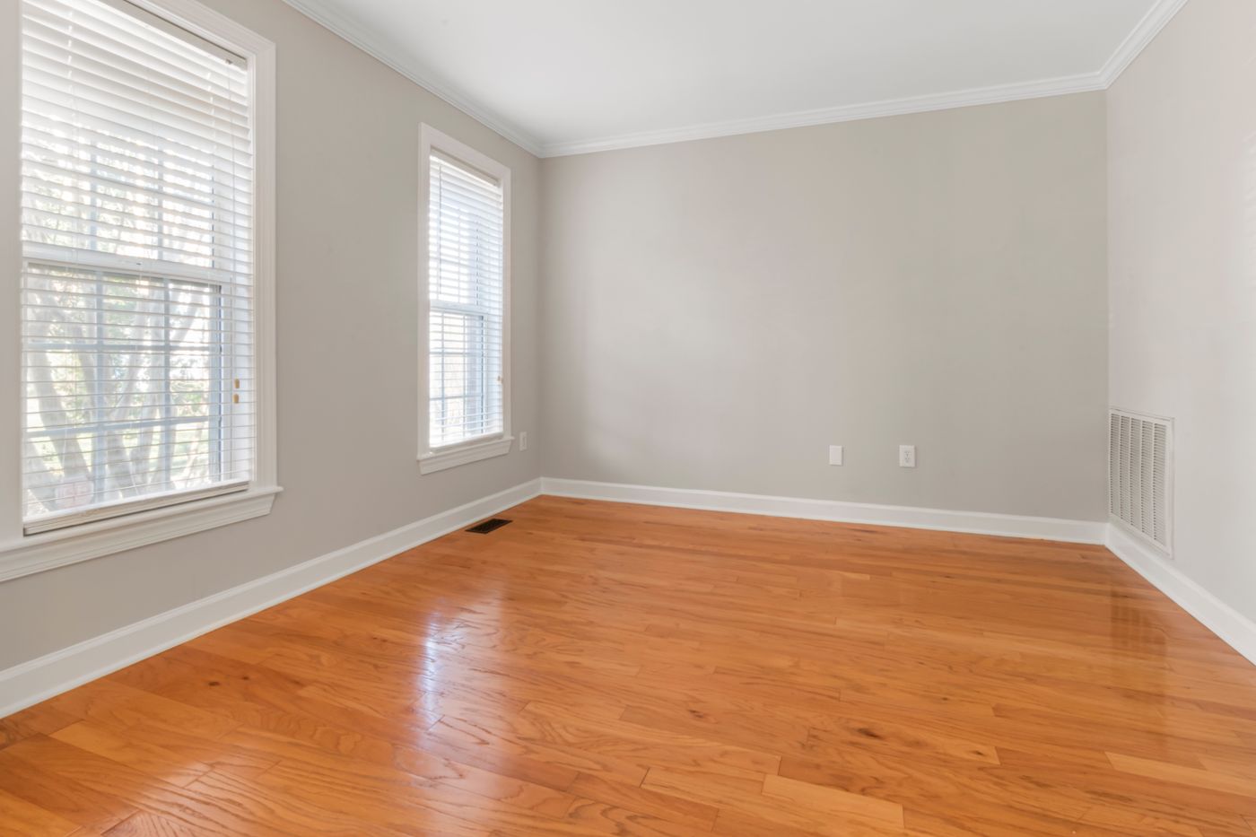 A bright empty room with newly laid hardwood flooring and fresh white walls